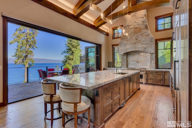 kitchen featuring sink, beamed ceiling, light hardwood / wood-style flooring, an island with sink, and a water view