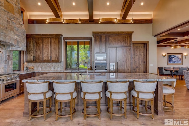 kitchen featuring light wood-type flooring, beam ceiling, built in appliances, and a large island