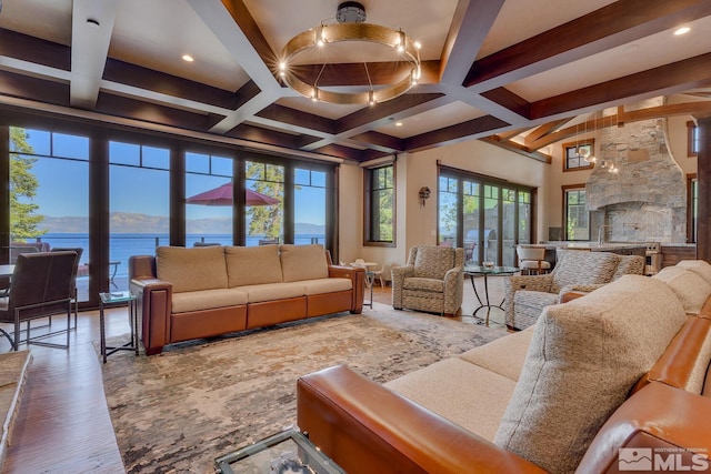 living room featuring beam ceiling, hardwood / wood-style floors, coffered ceiling, a water view, and a stone fireplace