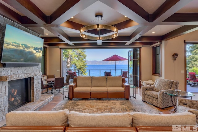 living room with beam ceiling, a water view, a stone fireplace, and coffered ceiling