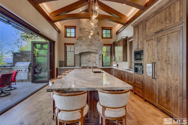 kitchen featuring sink, light wood-type flooring, a large island with sink, plenty of natural light, and oven