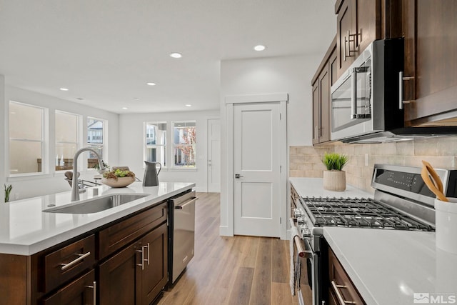 kitchen with dark brown cabinetry, stainless steel appliances, tasteful backsplash, sink, and light hardwood / wood-style floors