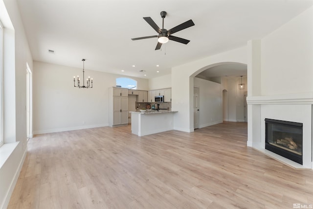 unfurnished living room with ceiling fan with notable chandelier and light hardwood / wood-style flooring