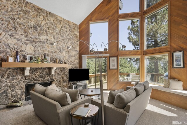 living room with wooden walls, carpet floors, high vaulted ceiling, and a stone fireplace