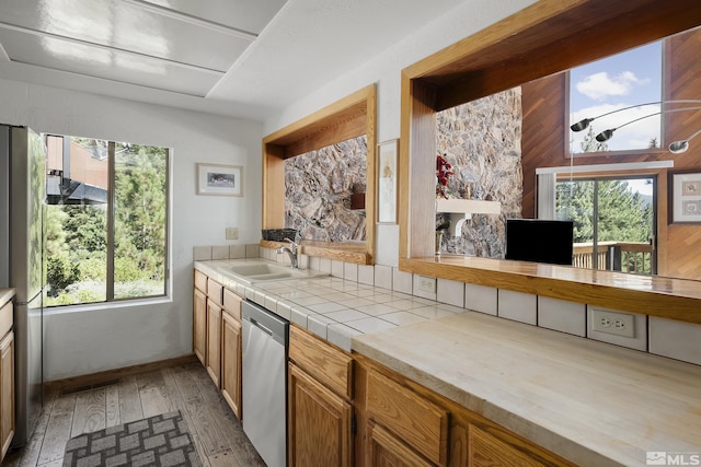 kitchen with stainless steel dishwasher, sink, tile countertops, and light hardwood / wood-style floors