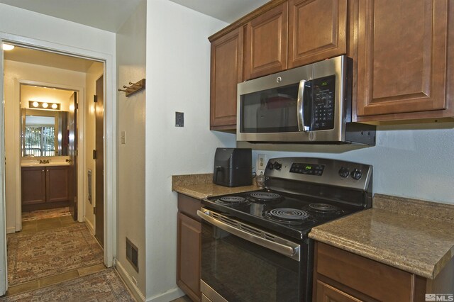 kitchen featuring stainless steel appliances, brown cabinetry, visible vents, and baseboards