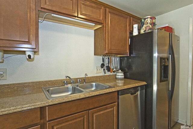 kitchen featuring appliances with stainless steel finishes, brown cabinetry, a sink, and light countertops