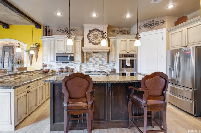 kitchen featuring dark stone counters, light wood-type flooring, backsplash, appliances with stainless steel finishes, and cream cabinetry