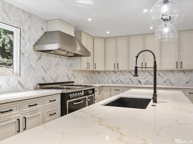 kitchen with wall chimney range hood, tasteful backsplash, range with two ovens, light stone counters, and decorative light fixtures