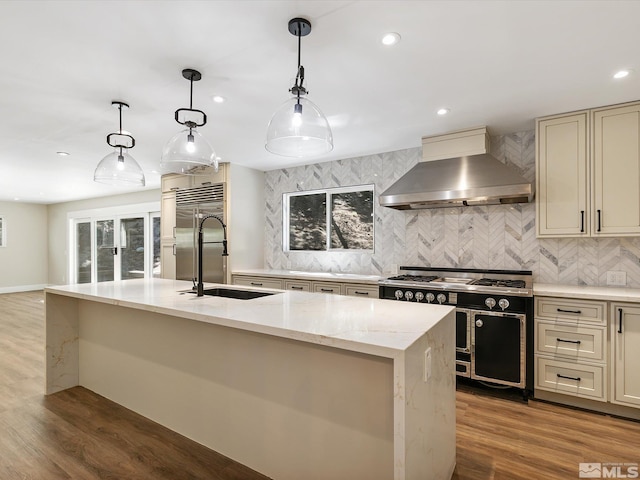 kitchen with a kitchen island with sink, backsplash, wood-type flooring, and wall chimney exhaust hood