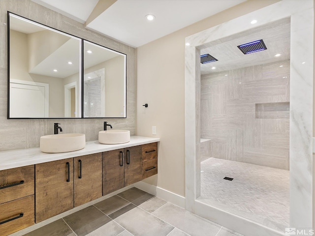 bathroom with dual vanity, a shower, tile patterned flooring, and tile walls