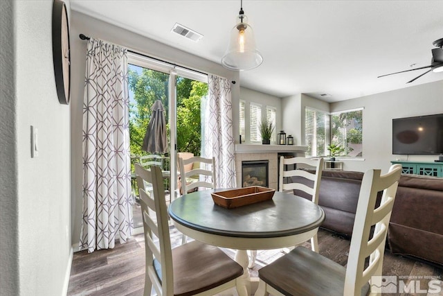 dining space with wood finished floors, a fireplace, visible vents, and ceiling fan