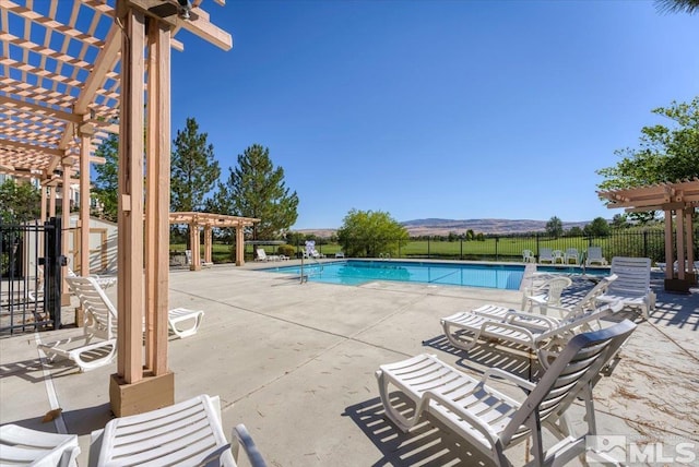 community pool with a patio area, a mountain view, fence, and a pergola