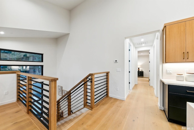 interior space featuring light wood-type flooring, baseboards, visible vents, and an upstairs landing