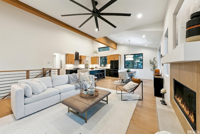 living room featuring light wood finished floors, a glass covered fireplace, beamed ceiling, high vaulted ceiling, and recessed lighting