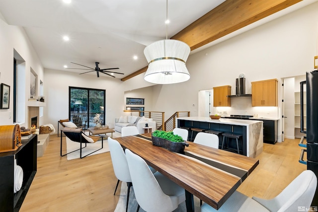 dining space featuring a lit fireplace, beamed ceiling, light wood-style flooring, and recessed lighting