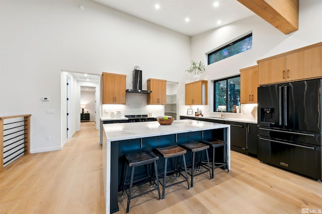 kitchen with a kitchen breakfast bar, black appliances, wall chimney range hood, and a center island