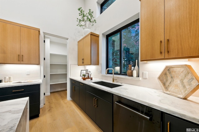 kitchen featuring a sink, light stone countertops, light wood-type flooring, dark cabinetry, and dishwasher