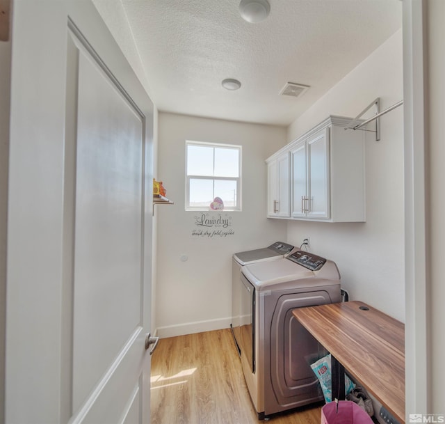 laundry area featuring washing machine and clothes dryer, a textured ceiling, light hardwood / wood-style flooring, and cabinets