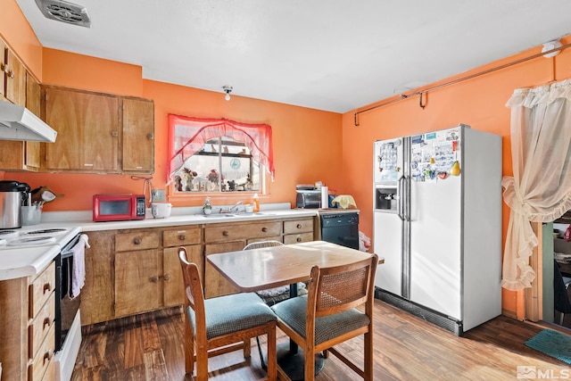 kitchen with light countertops, white appliances, brown cabinetry, and a sink