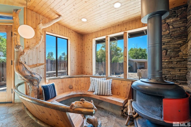 living area featuring stone tile floors, a wealth of natural light, a wood stove, wooden walls, and wooden ceiling