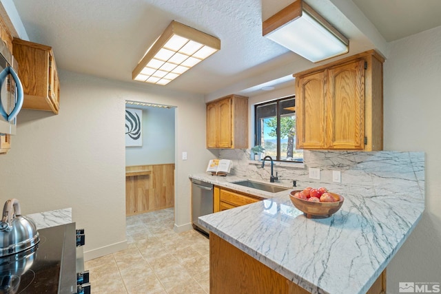 kitchen featuring decorative backsplash, brown cabinetry, a peninsula, a sink, and stainless steel dishwasher