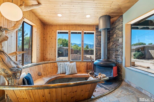 sunroom / solarium featuring a wealth of natural light, wooden ceiling, a mountain view, and a wood stove