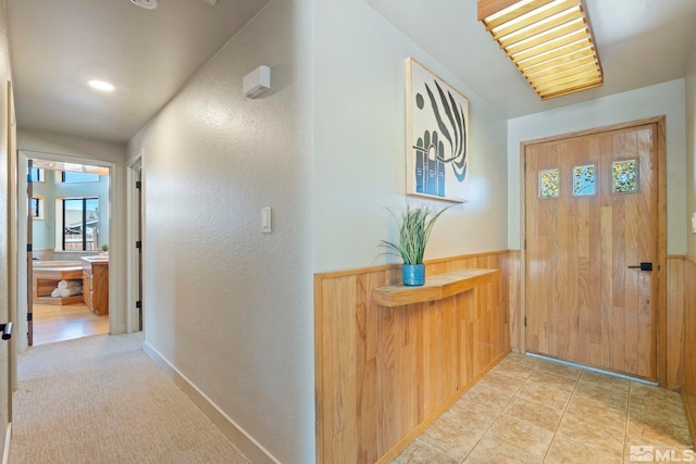 corridor featuring light tile patterned floors, wooden walls, and wainscoting