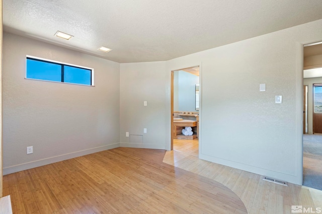 spare room featuring light wood-style floors, visible vents, a textured ceiling, and baseboards