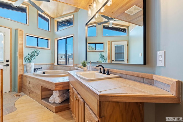 bathroom with ceiling fan, high vaulted ceiling, a bathtub, and vanity