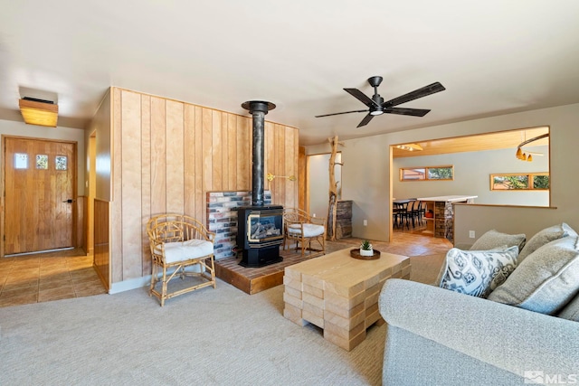 living area featuring light carpet, a wood stove, and a ceiling fan