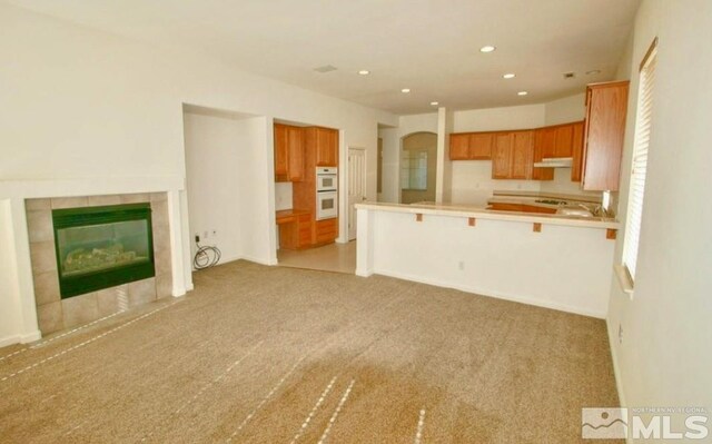 kitchen with a fireplace, kitchen peninsula, light carpet, and double oven