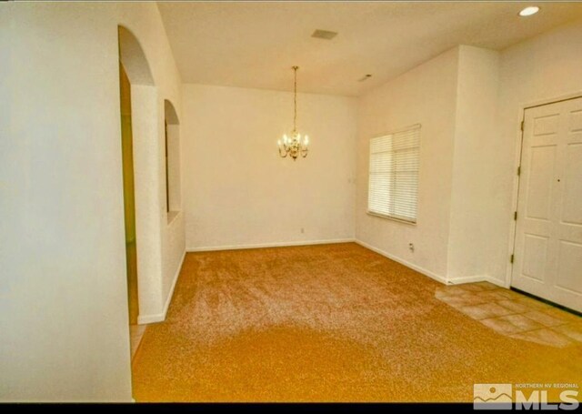 carpeted spare room featuring a notable chandelier