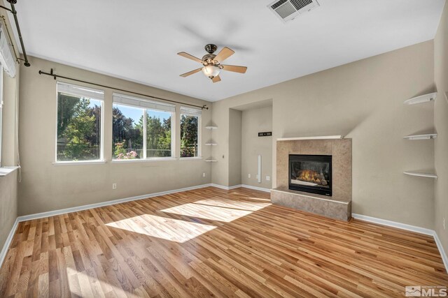 unfurnished living room with light hardwood / wood-style floors, a tile fireplace, and ceiling fan