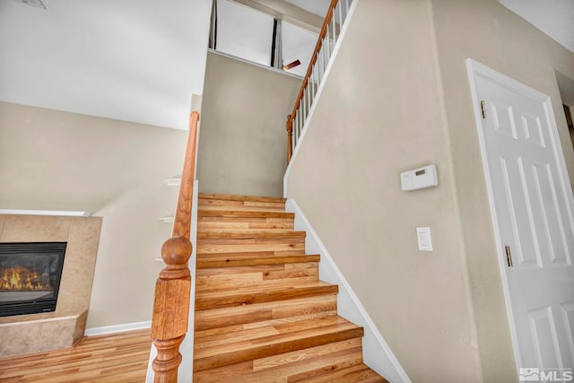 staircase featuring a fireplace, baseboards, and wood finished floors