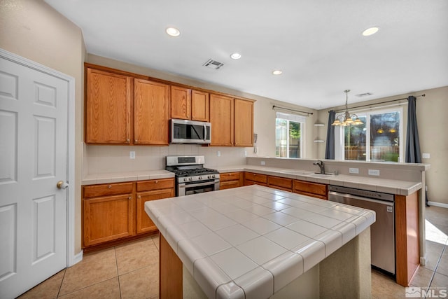 kitchen featuring tile countertops, stainless steel appliances, a peninsula, a sink, and visible vents