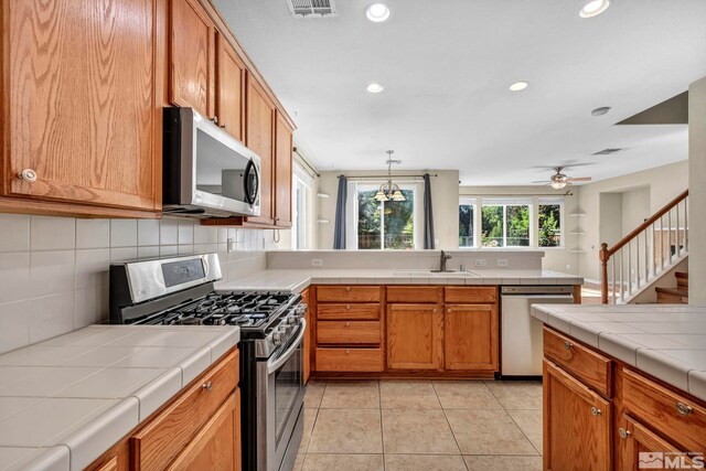 kitchen featuring ceiling fan, decorative backsplash, light tile patterned floors, tile countertops, and stainless steel appliances