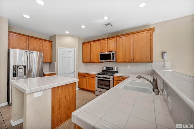 kitchen featuring a kitchen island, appliances with stainless steel finishes, tile countertops, sink, and light tile patterned flooring