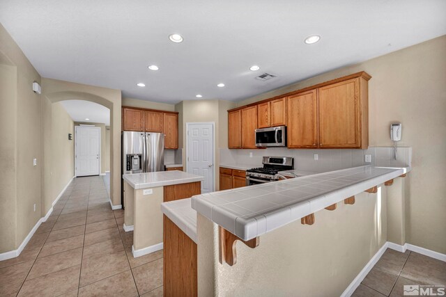 kitchen featuring a breakfast bar area, appliances with stainless steel finishes, light tile patterned floors, tile countertops, and kitchen peninsula