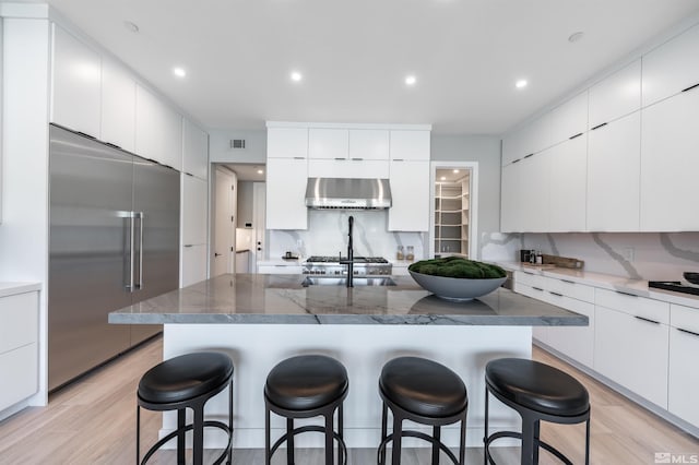 kitchen featuring built in refrigerator, tasteful backsplash, white cabinetry, and wall chimney exhaust hood