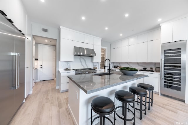 kitchen with wall chimney range hood, sink, light hardwood / wood-style floors, and high end refrigerator