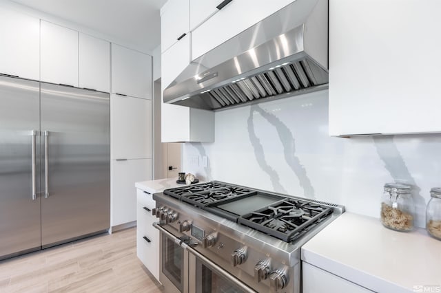 kitchen featuring light wood-type flooring, high end appliances, wall chimney range hood, and white cabinets