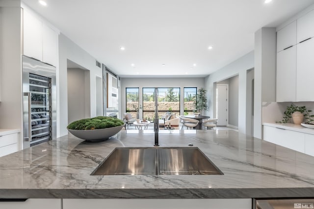 kitchen with white cabinets, beverage cooler, and light stone countertops