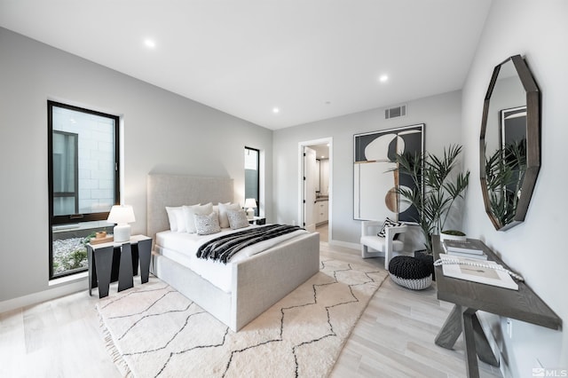 bedroom featuring light hardwood / wood-style floors, ensuite bath, and multiple windows