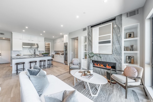 living room with sink, built in features, a high end fireplace, and light wood-type flooring