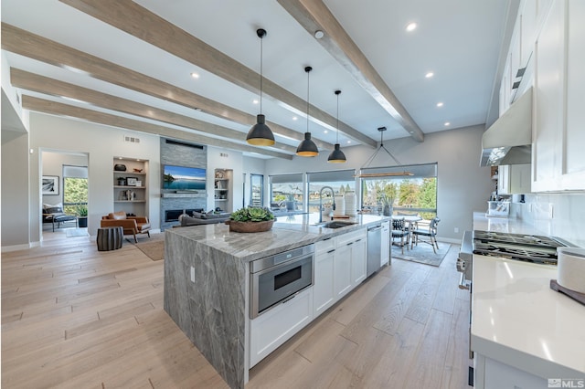 kitchen featuring white cabinets, a large island, hanging light fixtures, under cabinet range hood, and a sink