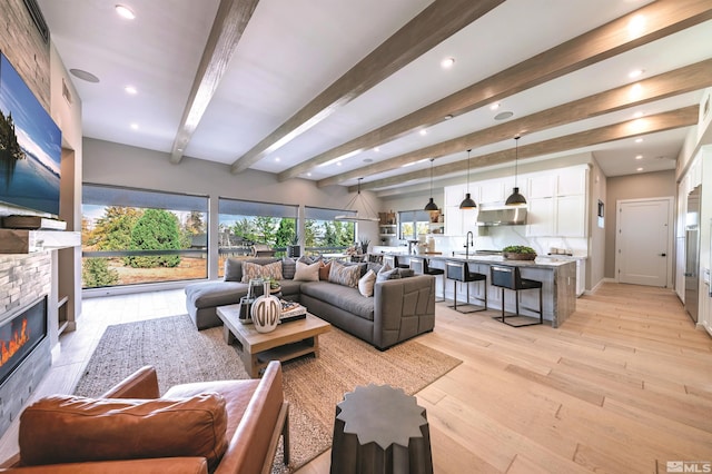 living room with recessed lighting, light wood-style flooring, beam ceiling, and a stone fireplace