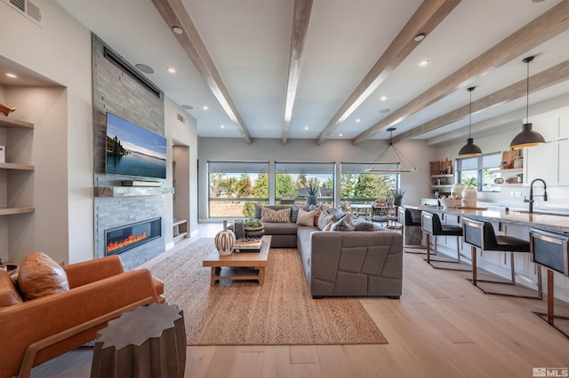 living area with a stone fireplace, recessed lighting, visible vents, light wood-style floors, and beam ceiling