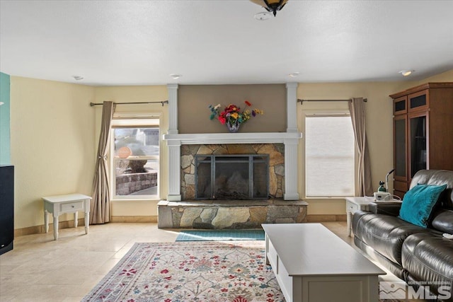 living room with a stone fireplace, baseboards, and light tile patterned floors