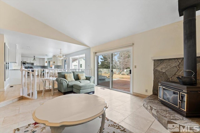 living room with a notable chandelier, a wood stove, light tile patterned flooring, vaulted ceiling, and baseboards